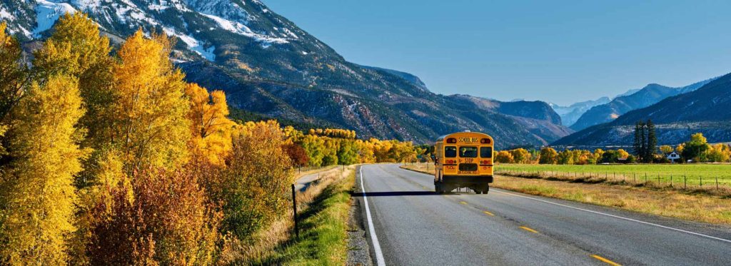 School bus on a mountain road lined with autumn aspens in Colorado
