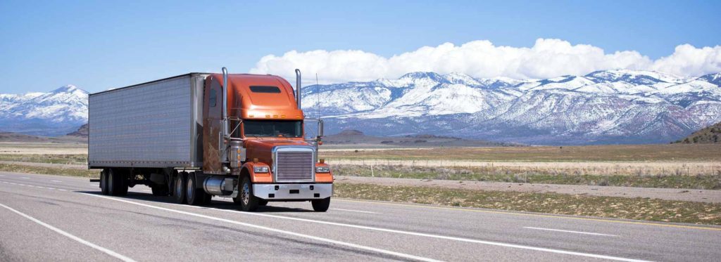 Semi-truck on a highway below snow-capped mountains in Utah